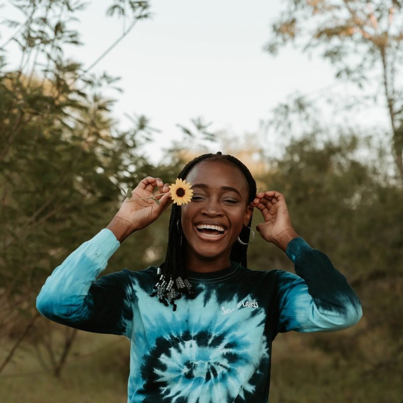 A young woman laughing, holding a sunflower over one eye